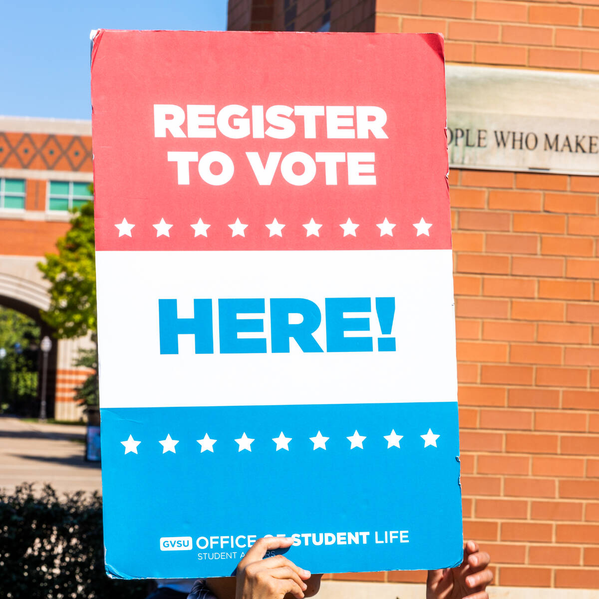 A red, white, and blue sign that says "Register to vote here!"